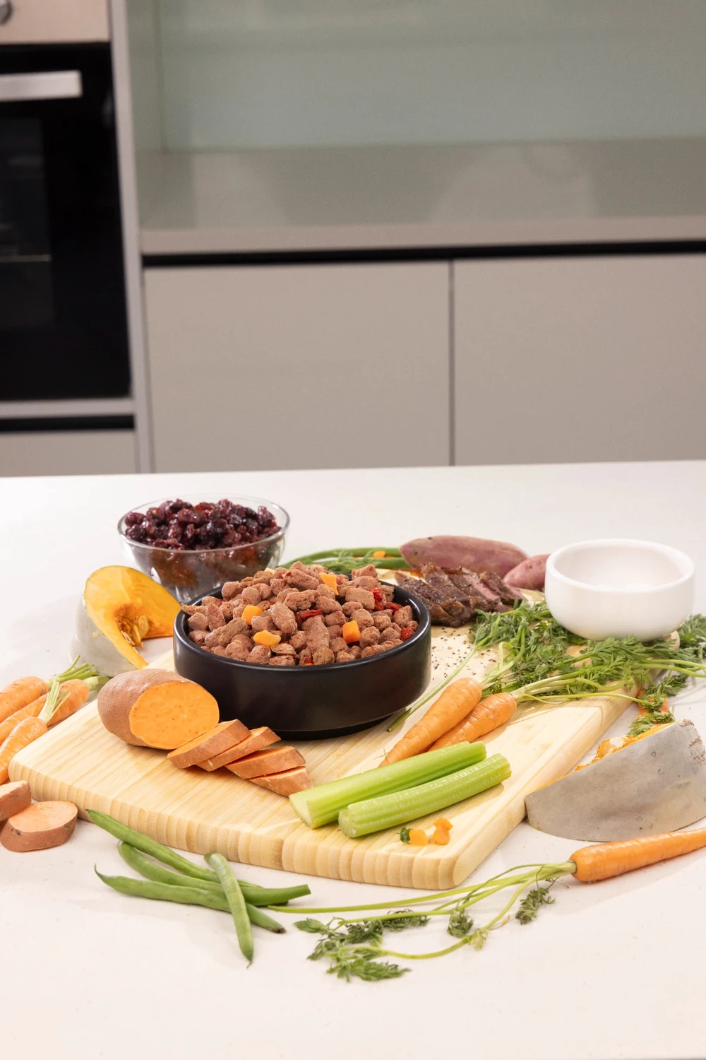 Fresh pet food bites in a bowl with meat, vegetables and fruit on a kitchen bench